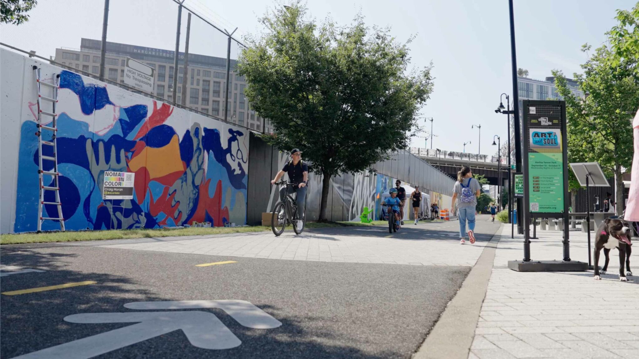 A photo showing a bike path with pedestrians and bikers in front of a colorful mural